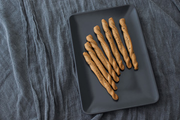 Delicious bread sticks standing on black plate, grey background