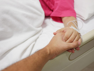 Hand of a man holding the hand of sickness woman that lying on a patient bed in the hospital