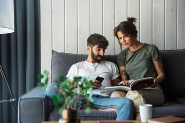Lovely young couple relaxing on a couch at home, reading magazine