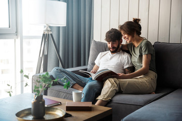 Lovely young couple relaxing on a couch at home, reading magazine