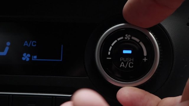 Close-up of pushing a button to turn on the air conditioner in a car. The mans hand turns the button and adjusts the comfort in the car