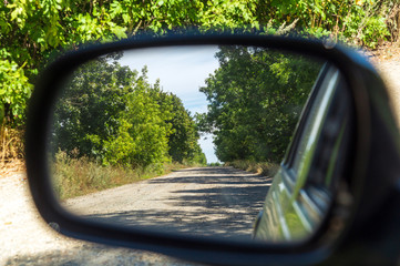 Rearview car driving mirror view green forest and village road.