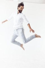 high key photo of a bearded man with brown hair who jumps on a white background, he is wearing a white linen shirt and blue pants - 372689630