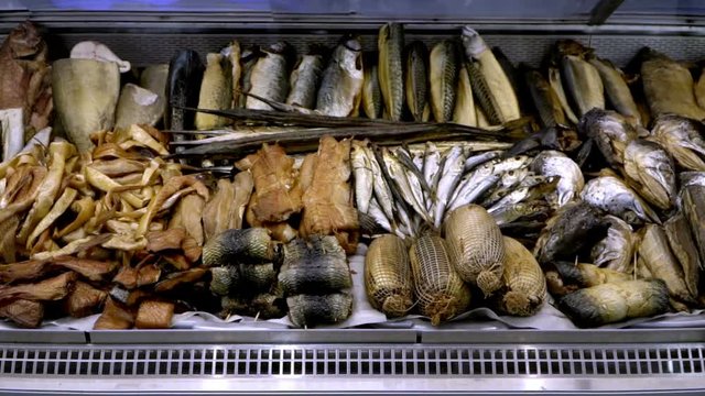 Close-up view of salted, dried, smoked fish and various seafood for sale in a supermarket showcase, slow motion