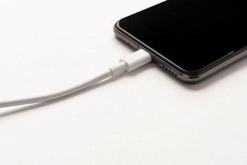 Charger with USB Type C cable and phone port. Smartphone close up on white background