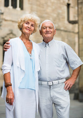 Portrait of cheerful positive senior man and woman in love holding hands strolling along city streets