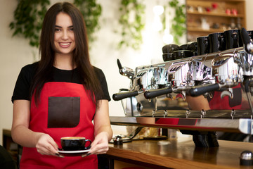 Portrait of attractive experienced barista with black hair standing at working place near coffee...