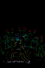 Silhouettes of people in glowing suits on a black background. Neon suit. Entertainment. Dancing.
