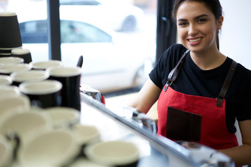 Portrait of cheerful owner of coffee shop in apron preparing beverages on professional equipment...