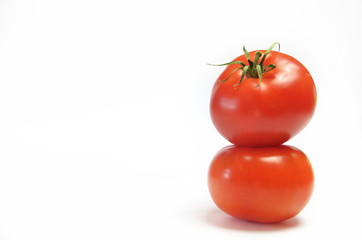 Two red tomatoes standing on top of each other against a white background