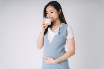 Beautiful pregnant asian woman with a cup of fresh isolate over white background.