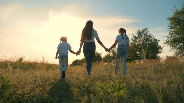 Happy family.A young mother walks with her children in a field at sunset. Two cute girls hold the hand of their mother, sister, teacher