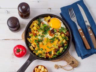 Fried eggs with potato in cast iron pan.