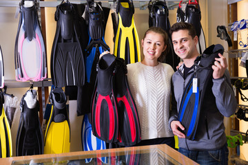 Glad cheerful positive man and woman are standing with modern diving flippers in the store. © JackF