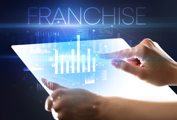 Hand holding futuristic tablet with FRANCHISE inscription above, modern business concept