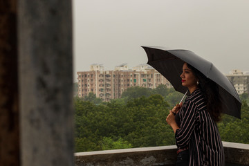 Indian woman with umbrella in the rain. looking at camera.