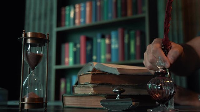 Pouring sand in an hourglass standing in an old library or study room. Vintage Concept