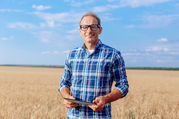 Portrait of farmer standing in a wheat field with a tablet looking at the camera