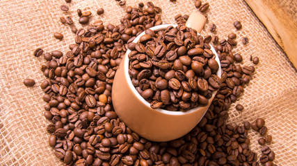 Mug full of coffee beans on the background of the bag,large Plenum