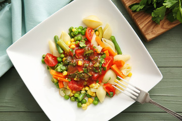 Plate with tasty conchiglie pasta and vegetables on table