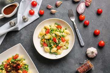 Plates with tasty conchiglie pasta and vegetables on dark background