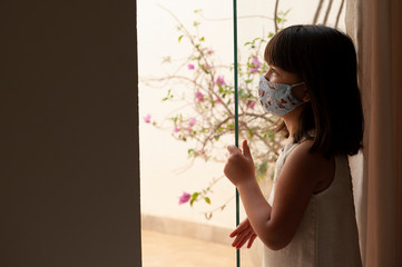 .New normal. Asian-looking girl wearing a mask to protect herself from Covid-19 or a corona virus looking out the window.