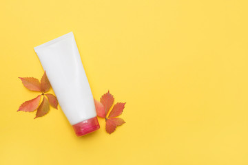 body cream on yellow background with red dry leaves, copy space