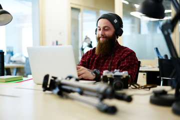 Positive male creating music using application on laptop computer and enjoying made composition via...
