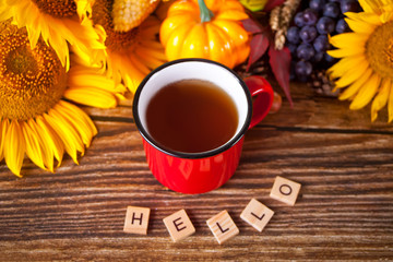 Greeting autumn card. Composition with pumpkin, autumn leaves, sunflower, red mug of tea and wooden text Hello on the wooden background. Cozy autumn mood concept.