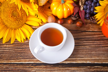 Greeting autumn card. Composition with pumpkin, autumn leaves, sunflower, cup of tea, plaid and berries on the wooden background. Cozy autumn mood concept.