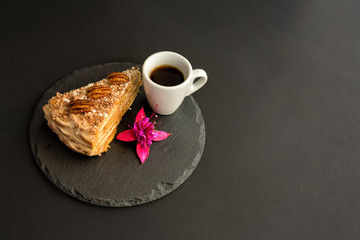 A typical Portuguese cake made of cookies called Bolo de Bolasa with cream, pecans, black and white chocolate on a black slate with espresso cup and a flower on a black background. Free space for text