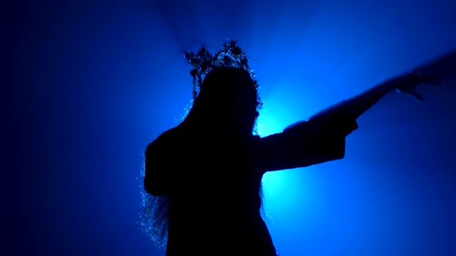 Black silhouette of a woman in the crown of a Chinese princess on a bright blue background. Smooth hand movements. Close up.