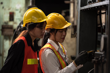 Portrait of young  Asian technician women or industrial worker with hardhat and vest working machine in Factory of manufacturing place  on Background