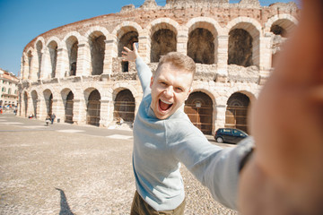 Happy male traveler makes selfie photo on background of amphitheater coliseum in city Verona Italy. Concept travel