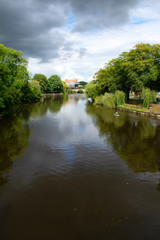 Fototapeta na wymiar The river Severn flowing through the beautiful English town of Shrewsbury. A summers scene with green parkland at the riverbank. Trees are reflected on the calm river waters. Copy space.