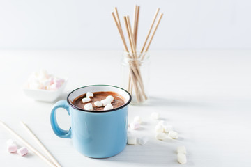 Hot chocolate with marshmallows in a blue enamel mug on white table.