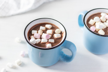 Hot chocolate with marshmallows in a blue enamel mug on white table.