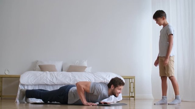 Family fitness at home, Father coach, Sports kid, Fun gymnastics. Dad teaches son to do push-ups from the floor at home