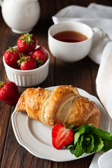 Fresh golden croissants with strawberries on dark slate board. Breakfast time. Top view