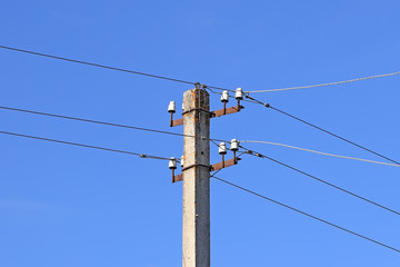 old concrete electric pole among trees against a blue sky