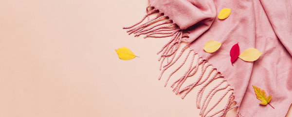 Pink cozy scarf with tassels and scattered leaves on pastel banner