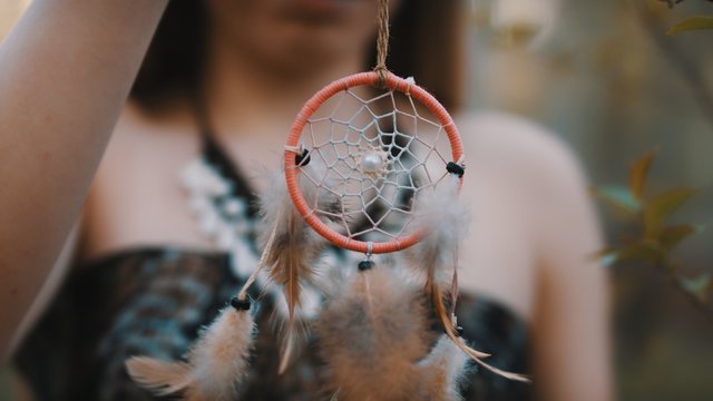 Young beautiful and mysterious woman holding dreamcatcher in the forest. No face, slow motion. High quality photo
