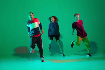Action time. Stylish men and woman dancing hip-hop in bright clothes on green background at dance hall in neon light. Youth culture, movement, style and fashion, action. Fashionable portrait.