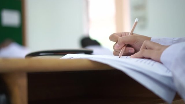 Student hand testing doing test exam with pencil drawing selected choices on answer sheet in school final exams at college or university. Taking multiple choice for assessment in examination classroom