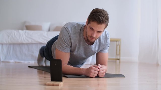 Family fitness at home, Father coach, Sports kid, Fun gymnastics. Attractive man doing sports exercise lying on the floor at home and timing the time on the smartphone
