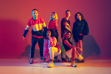 Young and crazy. Stylish men and woman dancing hip-hop in bright clothes on green background at dance hall in neon light. Youth culture, movement, style and fashion, action. Fashionable portrait.