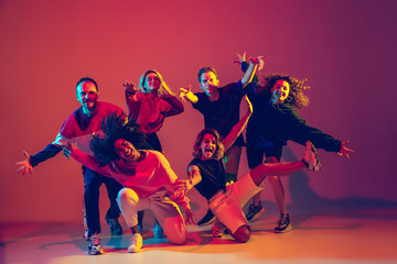 Young and crazy. Stylish men and woman dancing hip-hop in bright clothes on green background at dance hall in neon light. Youth culture, movement, style and fashion, action. Fashionable portrait.