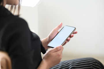Cropped image of the woman is using a mobile phone while sitting in the living room.