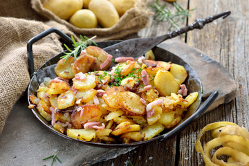 Deftige Bratkartoffeln mit Speck und Zwiebeln rustikal in der Eisenpfanne serviert – Hearty fried...