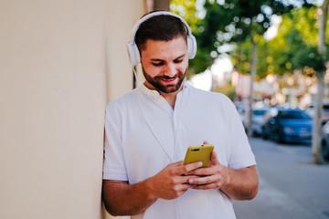 happy young man outdoors listening to music on mobile phone and headset. technology and lifestyle